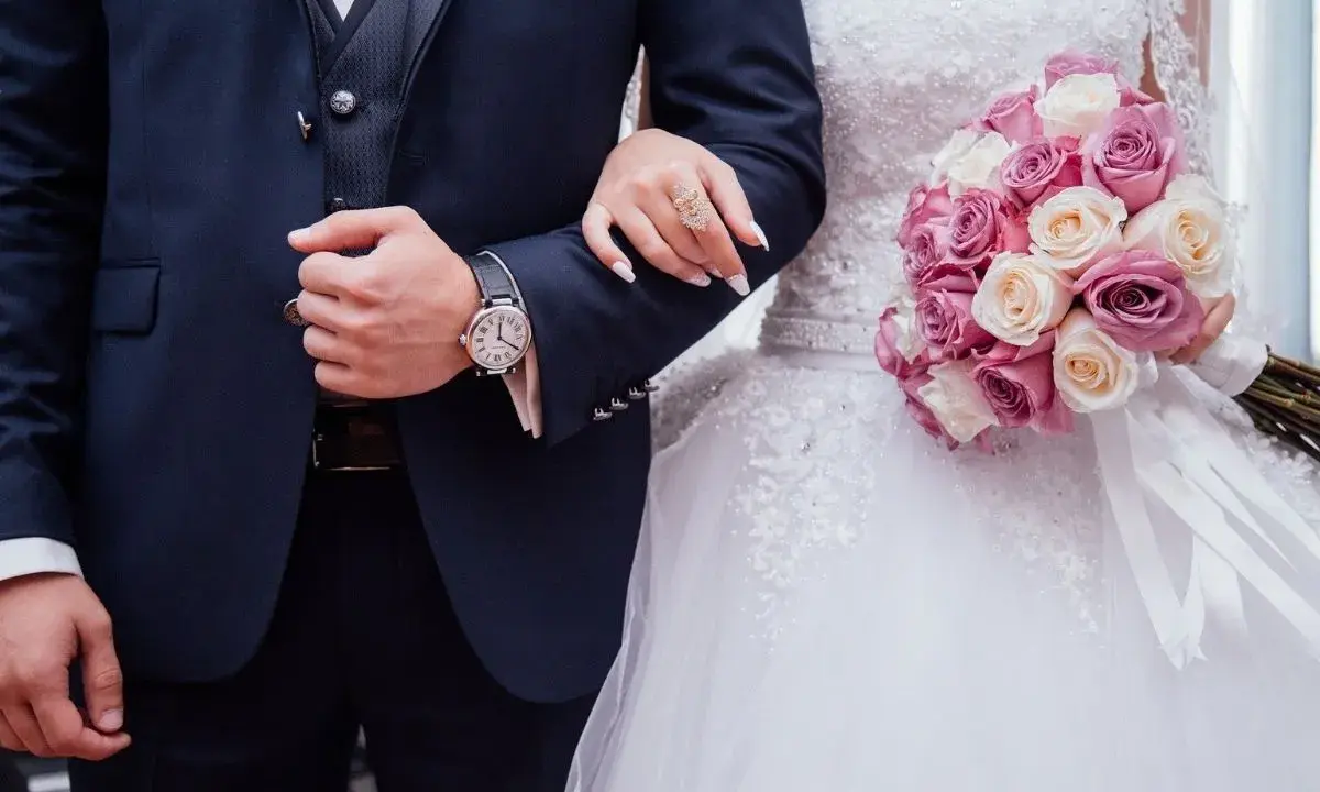Coppia di sposi con bouquet di rose. Lui indossa un orologio, lei un anello. Inizia il loro congedo matrimoniale CCNL Commercio.