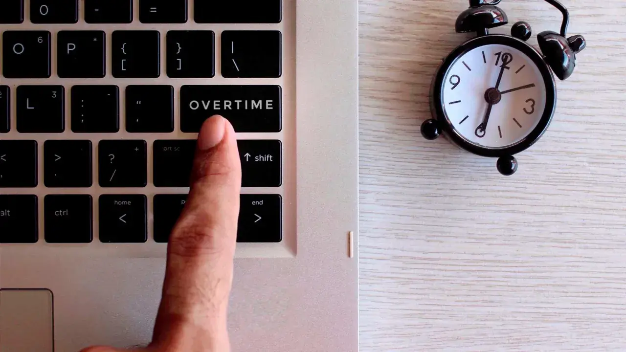 Dito, un dito preme il tasto "OVERTIME" su una tastiera, accanto a una sveglia. Quante ore di straordinario si possono fare in un mese?