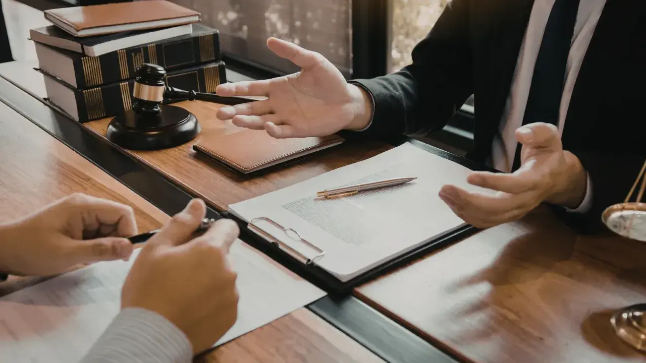 Consulenza legale: un avvocato, in veste di general counsel, spiega un contratto a un cliente, con martelletto e bilancia della giustizia sullo sfondo.