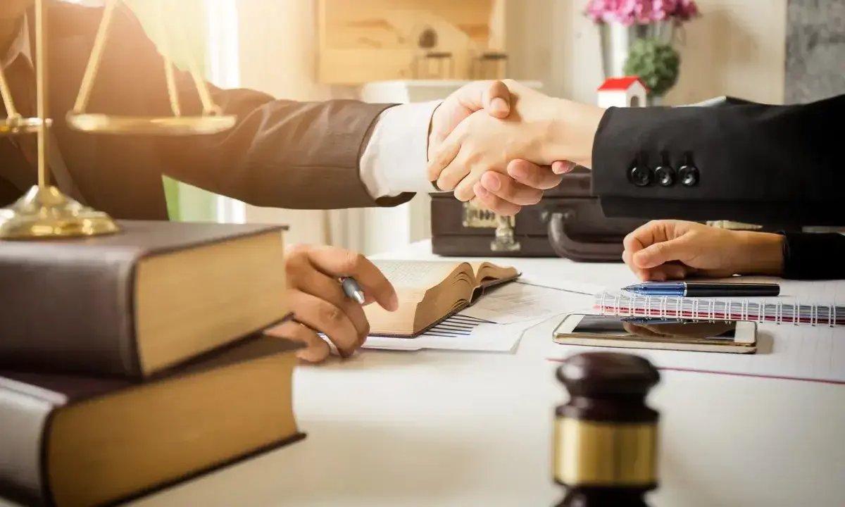 Avvocati si stringono la mano, simboli di giustizia e libri. La domanda "quanto guadagna un avvocato" è al centro di questo accordo.