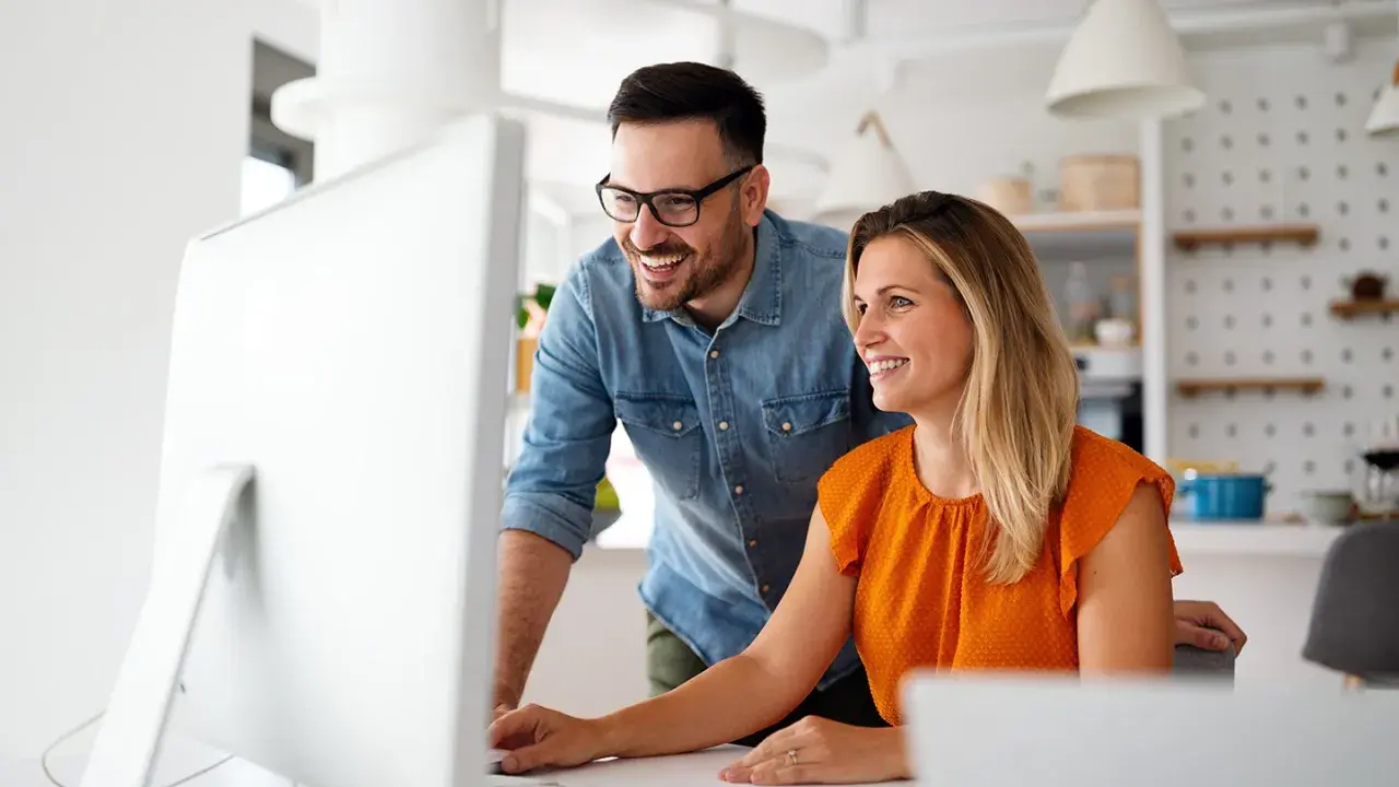 Coppia sorridente davanti al computer, forse scoprendo come funziona la banca ore per ottimizzare il lavoro.