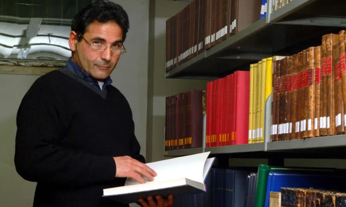 Uomo con occhiali in biblioteca, sfoglia un libro. Forse pensa al suo bibliotecario stipendio.