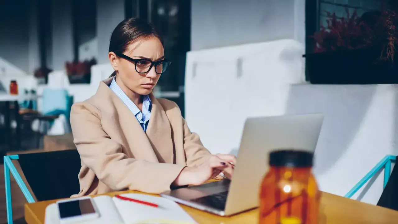 Donna con occhiali lavora al laptop, pensierosa sul gender pay gap in Italia.