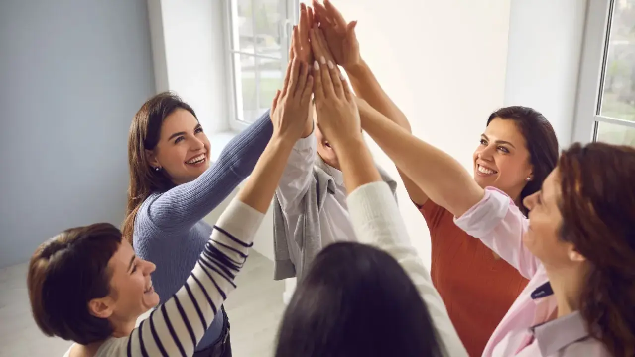 Un gruppo di donne sorridenti celebra il successo con un "high five" collettivo, simbolo di **empowerment femminile** e unione.