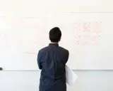 Uomo osserva schema su lavagna bianca, forse per un concorso INAIL. Disegni di interfacce e flusso di lavoro.