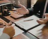 Consulenza legale: un avvocato, in veste di general counsel, spiega un contratto a un cliente, con martelletto e bilancia della giustizia sullo sfondo.