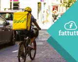 Corriere in bici con zaino giallo Glovo, pronto a consegnare. Scopri come lavorare con Glovo e unisciti alla squadra!