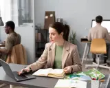 Donne al lavoro, forse preparano progetti per concorsi a Firenze. Uomini e donne concentrati sui loro computer, con mappe e quaderni aperti.