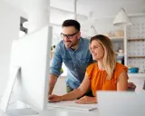 Coppia sorridente davanti al computer, forse scoprendo come funziona la banca ore per ottimizzare il lavoro.