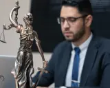 Statua della Giustizia e un uomo in giacca e cravatta, pronto per concorsi per laureati in giurisprudenza.