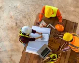 Operai edili discutono un grafico, forse relativo allo stipendio RSPP, su un cantiere.