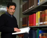 Uomo con occhiali in biblioteca, sfoglia un libro. Forse pensa al suo bibliotecario stipendio.
