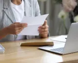 Persona esamina un documento, forse una busta paga contratto a chiamata, seduta alla scrivania con un laptop aperto.