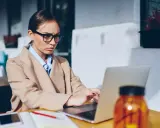 Donna con occhiali lavora al laptop, pensierosa sul gender pay gap in Italia.
