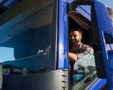 Un camionista sorridente al volante, pronto per un nuovo viaggio. Il suo stipendio camionista è meritato per il duro lavoro su strada.