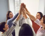Un gruppo di donne sorridenti celebra il successo con un "high five" collettivo, simbolo di **empowerment femminile** e unione.