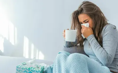Donna con fazzoletto e tazza, coperta da un plaid. Il suo tirocinio è interrotto da una malattia.