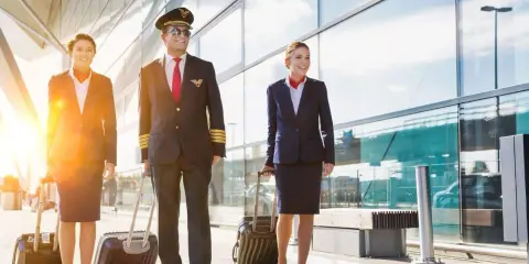 Equipaggio Ryanair cammina in aeroporto con valigie. Il pilota e le hostess sorridono, pensando al loro stipendio.