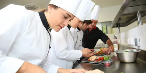 Giovani chef imparano da su chef chi è un maestro in cucina, preparando piatti raffinati.
