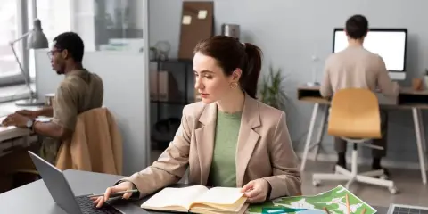 Donne al lavoro, forse preparano progetti per concorsi a Firenze. Uomini e donne concentrati sui loro computer, con mappe e quaderni aperti.
