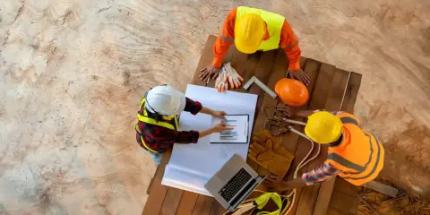 Operai edili discutono un grafico, forse relativo allo stipendio RSPP, su un cantiere.