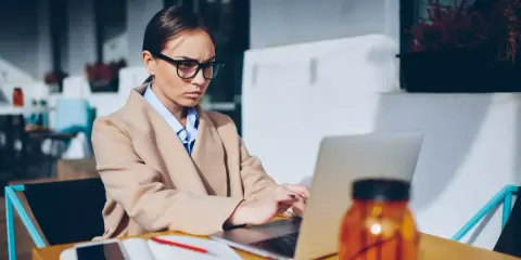 Donna con occhiali lavora al laptop, pensierosa sul gender pay gap in Italia.