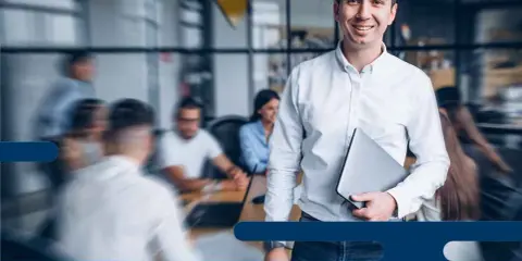 Uomo sorridente con laptop, pronto per l'induction aziendale. Inserire una nuova risorsa in un team è un processo chiave.