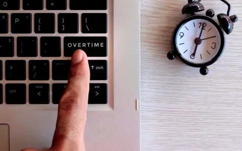 Dito, un dito preme il tasto "OVERTIME" su una tastiera, accanto a una sveglia. Quante ore di straordinario si possono fare in un mese?