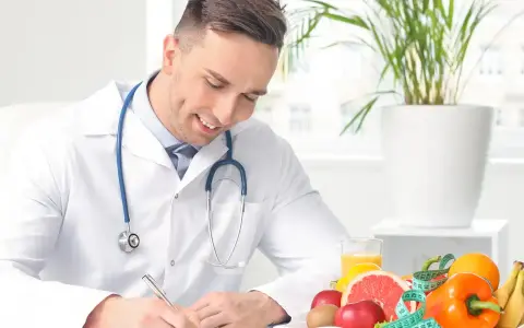 Medico sorridente con stetoscopio, circondato da frutta e verdura, mentre scrive. Un esempio di come diventare nutrizionista.