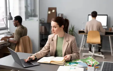 Donne al lavoro, forse preparano progetti per concorsi a Firenze. Uomini e donne concentrati sui loro computer, con mappe e quaderni aperti.