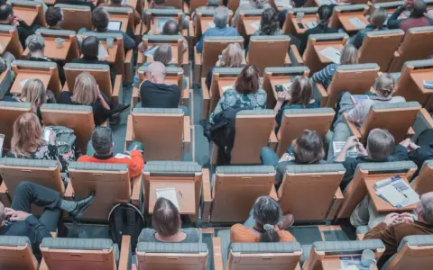 Un pubblico attento in un'aula, molti con quaderni e penne, pronti per nuovi concorsi non scaduti.