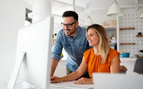Coppia sorridente davanti al computer, forse scoprendo come funziona la banca ore per ottimizzare il lavoro.