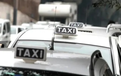 Code di taxi bianchi in attesa, un'immagine che fa riflettere su quanto guadagna un tassista.