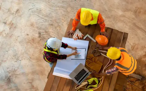 Operai edili discutono un grafico, forse relativo allo stipendio RSPP, su un cantiere.