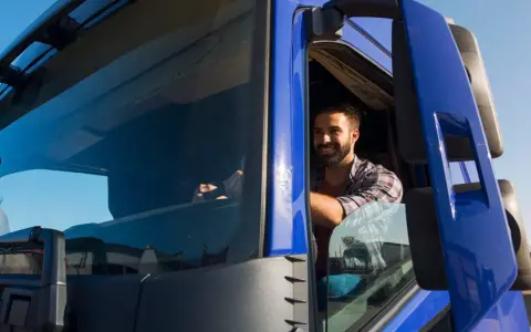 Un camionista sorridente al volante, pronto per un nuovo viaggio. Il suo stipendio camionista è meritato per il duro lavoro su strada.
