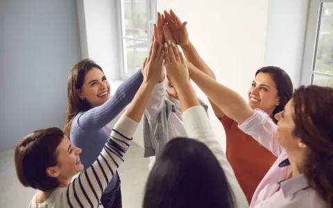 Un gruppo di donne sorridenti celebra il successo con un "high five" collettivo, simbolo di **empowerment femminile** e unione.