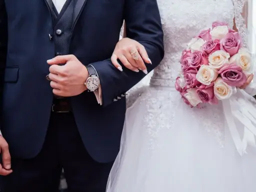 Coppia di sposi con bouquet di rose. Lui indossa un orologio, lei un anello. Inizia il loro congedo matrimoniale CCNL Commercio.