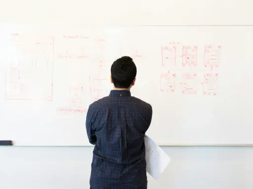 Uomo osserva schema su lavagna bianca, forse per un concorso INAIL. Disegni di interfacce e flusso di lavoro.