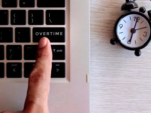 Dito, un dito preme il tasto "OVERTIME" su una tastiera, accanto a una sveglia. Quante ore di straordinario si possono fare in un mese?