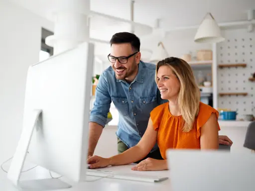 Coppia sorridente davanti al computer, forse scoprendo come funziona la banca ore per ottimizzare il lavoro.