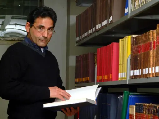 Uomo con occhiali in biblioteca, sfoglia un libro. Forse pensa al suo bibliotecario stipendio.