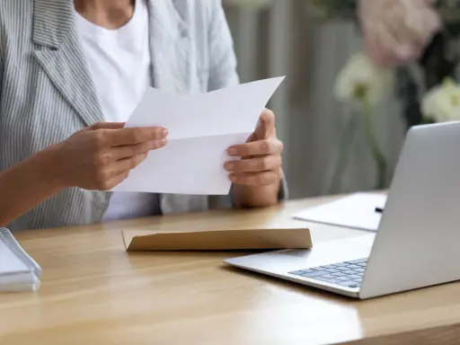 Persona esamina un documento, forse una busta paga contratto a chiamata, seduta alla scrivania con un laptop aperto.