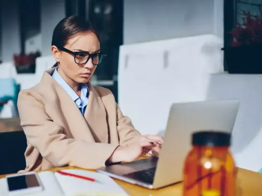 Donna con occhiali lavora al laptop, pensierosa sul gender pay gap in Italia.