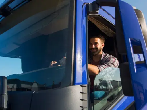 Un camionista sorridente al volante, pronto per un nuovo viaggio. Il suo stipendio camionista è meritato per il duro lavoro su strada.