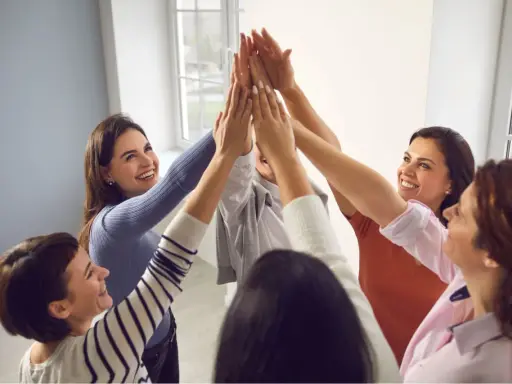 Un gruppo di donne sorridenti celebra il successo con un "high five" collettivo, simbolo di **empowerment femminile** e unione.