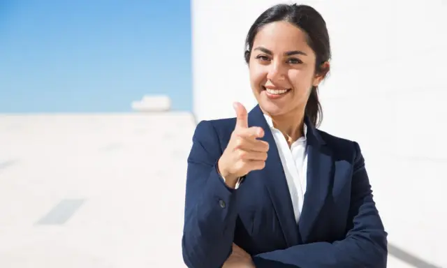 Donna in giacca blu indica con il dito, sorridendo. Un'immagine che simboleggia il ruolo di un hr business partner cosa fa: connette persone e obiettivi.