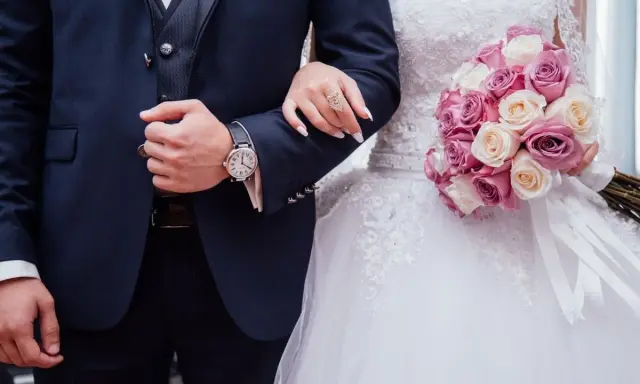 Coppia di sposi con bouquet di rose. Lui indossa un orologio, lei un anello. Inizia il loro congedo matrimoniale CCNL Commercio.