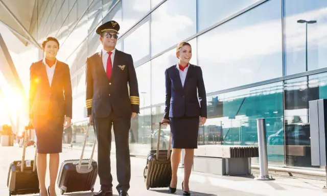 Equipaggio Ryanair cammina in aeroporto con valigie. Il pilota e le hostess sorridono, pensando al loro stipendio.