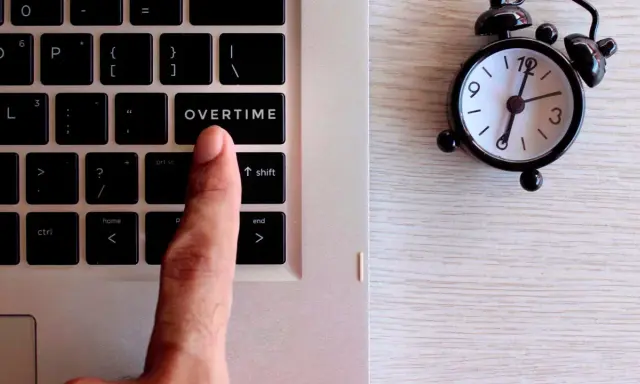 Dito, un dito preme il tasto "OVERTIME" su una tastiera, accanto a una sveglia. Quante ore di straordinario si possono fare in un mese?