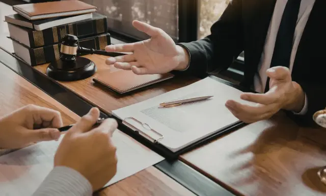 Consulenza legale: un avvocato, in veste di general counsel, spiega un contratto a un cliente, con martelletto e bilancia della giustizia sullo sfondo.
